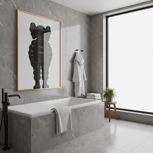 May include: A modern bathroom with a white bathtub, a large framed artwork, and a window. The artwork features a black and white figure. A white robe hangs on the wall, and a small wooden stool holds a plant. The walls and floor are gray.