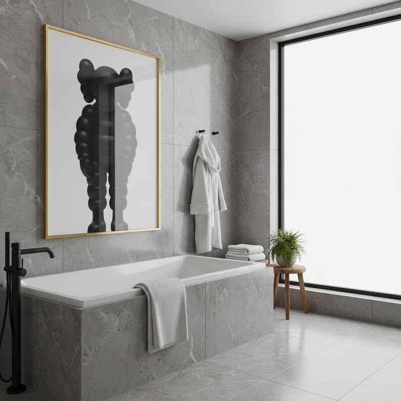 May include: A modern bathroom with a white bathtub, a large framed artwork, and a window. The artwork features a black and white figure. A white robe hangs on the wall, and a small wooden stool holds a plant. The walls and floor are gray.