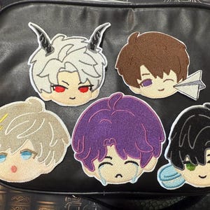 May include: Five embroidered patches featuring anime-style character faces with various hair colors and expressions. One has horns and red eyes, another has a paper airplane, and one is crying. The patches are on a black bag.