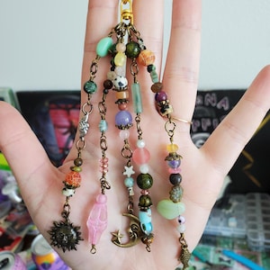 May include: A multi-strand beaded keychain featuring a gold-tone lobster clasp. The strands are adorned with various colorful gemstone beads, small metal spacers, and charms including a sun, a crescent moon, and a small fish figure.