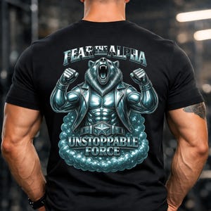 Può includere: T-shirt nero con una grafica di un orso con un fisico muscoloso, che indossa una giacca e ruggisce. Il testo "FEAR THE ALPHA" è sopra l'orso e "UNSTOPPABLE FORCE" sotto. Il design è in tonalità blu e argento.