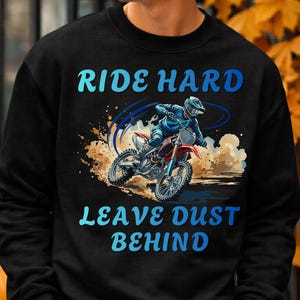 Peut inclure: Un sweat-shirt noir à col rond avec un motif représentant un pilote de motocross sur une moto rouge et blanche soulevant de la poussière. Le texte RIDE HARD est imprimé en bleu au-dessus et LEAVE DUST BEHIND est imprimé en bleu en dessous.