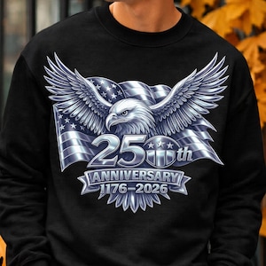 Peut inclure: Sweat-shirt noir avec un motif argenté d'un aigle aux ailes déployées, un drapeau américain et le texte "25th Anniversary 1776-2026". Le motif est centré sur la poitrine.