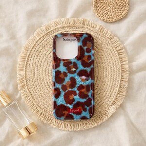 May include: A phone case with a leopard print design in brown and blue. The case has the word "Instagram" printed at the top and "Leopard" at the bottom. The case is on a woven placemat.