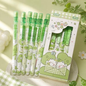 May include: A set of six green mechanical pencils with white barrels featuring cartoon cat illustrations and star patterns, accompanied by a rectangular cardboard box labeled 4PCS with matching green cat graphics and text in Chinese characters.