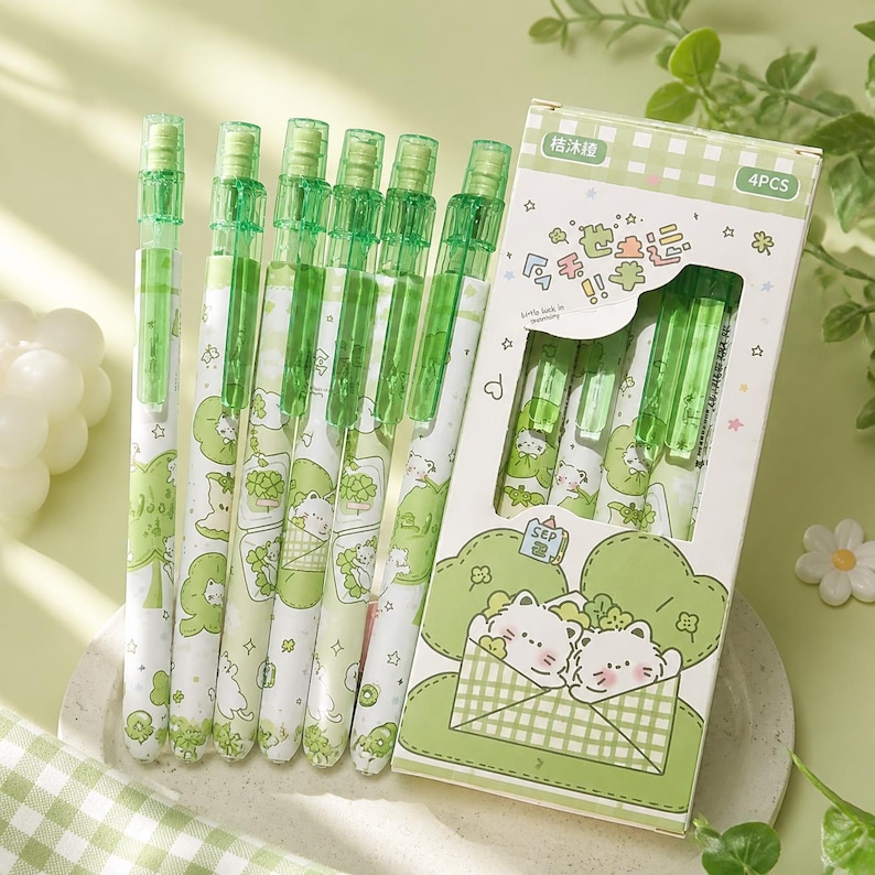 May include: A set of six green mechanical pencils with white barrels featuring cartoon cat illustrations and star patterns, accompanied by a rectangular cardboard box labeled 4PCS with matching green cat graphics and text in Chinese characters.