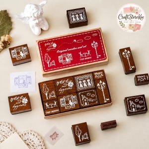Peut inclure: Un ensemble de neuf tampons en caoutchouc avec des motifs en ligne blanche représentant des chats, des réverbères, des maisons et des arbres. Les tampons sont rangés dans une boîte en carton rouge et marron marquée Original wooden seal set.