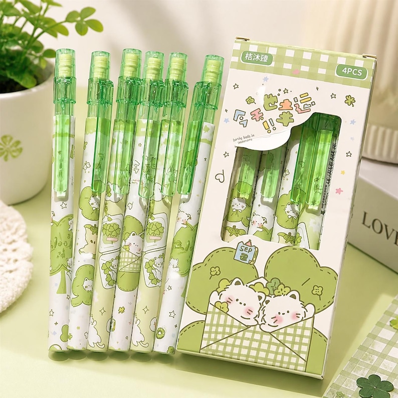 May include: A set of six mechanical pencils with translucent green clips and white barrels featuring illustrations of white cats and green clover patterns. The pencils are displayed alongside a rectangular cardboard box labeled 4PCS.