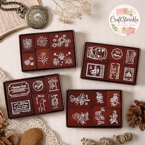 Può includere: Quattro scatole rettangolari in legno contenenti set di timbri in gomma. Ogni scatola presenta timbri con disegni a inchiostro bianco, tra cui fuochi d'artificio, illustrazioni di Venezia, etichette postali vintage e disegni botanici floreali.