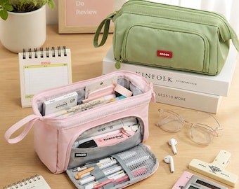May include: A light green rectangular pencil case with a red Angoo label and a matching open pink pencil case containing various pens, markers, and highlighters. The pink case features a front zippered compartment with mesh pockets and elastic loops.