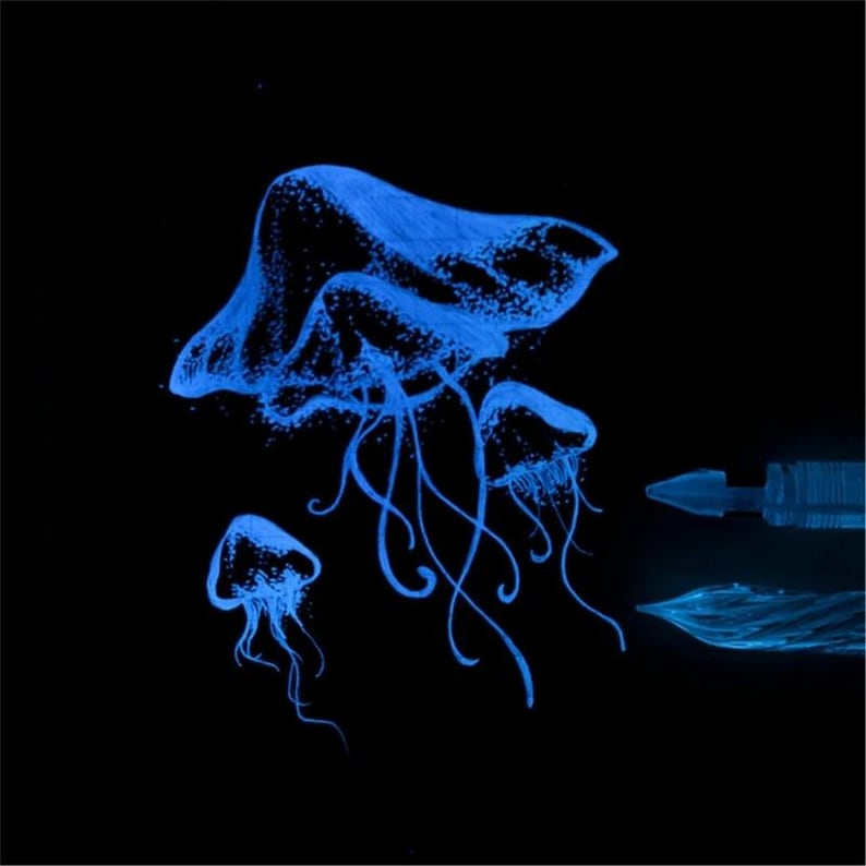 Puede incluir: Una ilustraci&oacute;n azul brillante de tres medusas sobre un fondo negro, con una medusa central grande y dos m&aacute;s peque&ntilde;as cerca. A la derecha, se ven dos plumines de pluma estilogr&aacute;fica distintos, tambi&eacute;n representados en un azul luminoso.