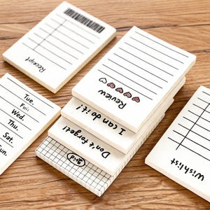 May include: Several small, white notepads with different designs and text are displayed. Some have lined pages, others feature grids or checklists. Text includes "Receipt," "Review," "I can do it!," and "Don't forget!" with heart and checkmark illustrations.