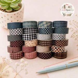 Peut inclure: Une collection de vingt-cinq rouleaux de ruban adhésif décoratif washi empilés. Les rubans présentent divers motifs, notamment vichy, tartan, rayures, pois et petits cœurs dans des tons de bleu, marron, rouge, noir et blanc.