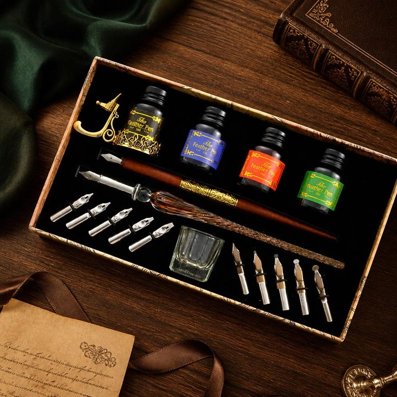 K&ouml;nnte beinhalten: Ein Kalligraphie-Set in einer rechteckigen Schachtel mit einem braun-goldenen F&uuml;llfederhalter, vier kleinen Tintenf&auml;ssern mit Etiketten der Aufschrift The Feather Pen, einer goldenen Stiftablage, einem kleinen Glas-Tintenfass und zehn silbernen Federn.