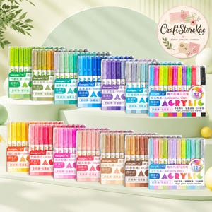 Op de afbeelding: Een collectie van twaalf sets acrylmarkers, elk met twaalf pennen in verschillende kleurenpaletten. De verpakking toont de merknaam GuangNa, de tekst ACRYLIC en specifieke kleurenserienamen zoals Fluorescent en Macaron.