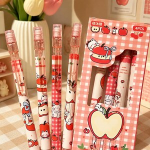 May include: Four mechanical pencils with white barrels featuring red apple and white cat illustrations, paired with a pink and white checkered cardboard box labeled 4PCS and Chinese text, displaying matching apple and cat graphic designs.