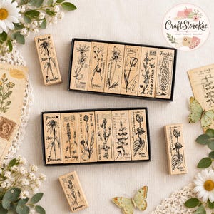 May include: A collection of rectangular wooden rubber stamps featuring black ink botanical illustrations and script text. The stamps are arranged in two black boxes and individually, showcasing various floral designs, leaves, and vintage-style postal markings.