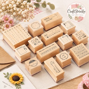 May include: A collection of light-colored wooden rubber stamps featuring various designs including a weekly planner, a clock, weather icons, a calendar grid, and text such as bedtime, story time, and week challenge, arranged on a textured surface.
