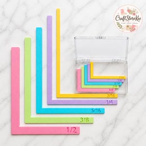 Pode incluir: Um conjunto de ferramentas de alinhamento de cantos em forma de L nas cores rosa, verde-limão, turquesa, roxo e amarelo. Cada ferramenta possui medidas fracionárias em relevo de 3/16, 1/4, 5/16, 3/8 e 1/2 polegada. Um estojo de plástico.