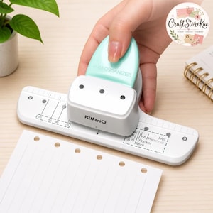 May include: A white and mint green KW-trio 6-hole paper punch with a guide plate featuring markings for A5, A6, Personal, Pocket, Mini, and A7 paper sizes. The tool has a rounded mint green handle and a white base with printed measurement guides.