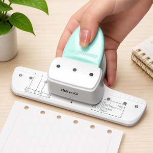 May include: A white and mint green KW-trio paper punch with a 4MM ORGANIZER handle. The base features printed markings for A7, A6, Personal, Pocket, Mini, and A5 paper sizes, along with a ruler scale. It is designed for creating holes in paper.