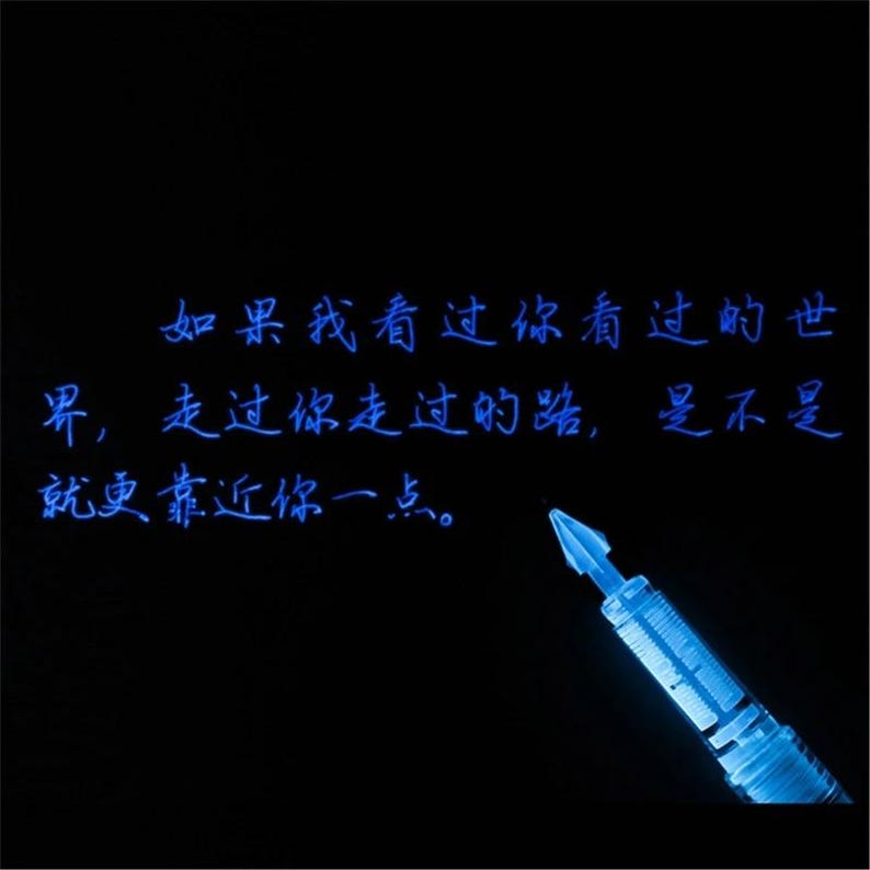 Puede incluir: Una punta de pluma estilogr&aacute;fica azul brillante situada en la esquina inferior derecha sobre un fondo negro. El texto "如果我看过你看过的世界，走过你走过的路，是不是就更靠近你一点。" est&aacute; escrito en una caligraf&iacute;a azul luminosa sobre la superficie oscura.