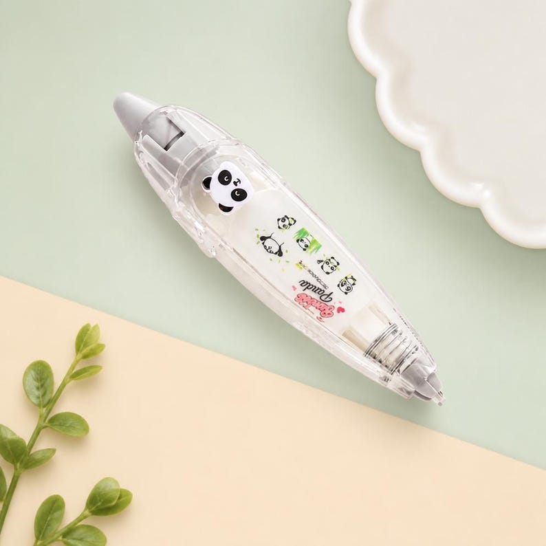 Puede incluir: Un dispensador de cinta correctora transparente con tem&aacute;tica de panda. El dispensador tiene una punta gris y un rollo de cinta blanco. El cuerpo del dispensador est&aacute; decorado con ilustraciones de pandas y la palabra "Panda".