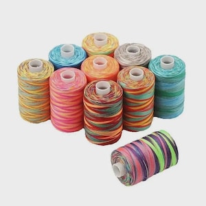 May include: A collection of colorful spools of thread. The spools are cylindrical with a white core and are wrapped with threads in various colors, including yellow, orange, pink, blue, and green. The threads are tightly wound, creating a textured appearance.