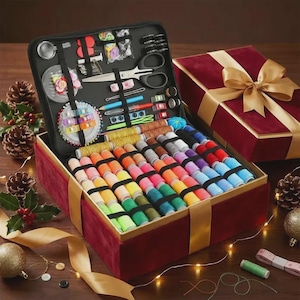 May include: A red velvet sewing kit with a gold ribbon, open to reveal a black zippered case filled with sewing tools. The kit includes scissors, spools of colorful thread, needles, and other accessories. A second gift box with a gold bow is in the background.