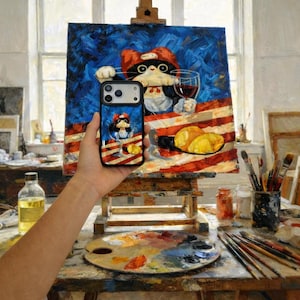 Può includere: Custodia nera per iPhone con un design a cartone animato di un gatto, tenuta davanti a un dipinto di un gatto con un cappello rosso che tiene un bicchiere di vino. Il dipinto è su un cavalletto nello studio di un artista.