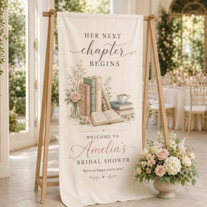 May include: A linen banner on a wooden easel with the text "HER NEXT chapter BEGINS" and "WELCOME TO Amelia's BRIDAL SHOWER". The banner features a watercolor illustration of books, flowers, and a teacup. A floral arrangement sits in front.