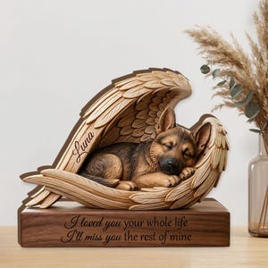 May include: A wooden memorial featuring a sleeping German Shepherd puppy nestled within carved angel wings. The name "Luna" is inscribed on the wing. The base has the text: "I loved you your whole life, I'll miss you the rest of mine."