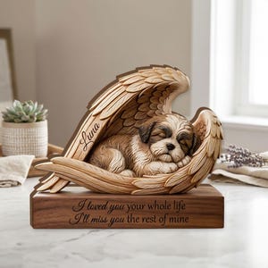 May include: A wooden memorial sculpture of a sleeping dog nestled in angel wings. The sculpture is brown and beige, with the dog's name "Luna" inscribed on the wing. The base reads "I loved you your whole life, I'll miss you the rest of mine."