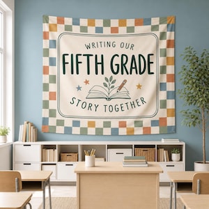 May include: A rectangular wall tapestry featuring a checkered border in muted tones of blue, green, orange, and yellow. The center displays the text "WRITING OUR FIFTH GRADE STORY TOGETHER" with an illustration of an open book and a pencil.