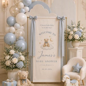 May include: A baby shower banner on a gold frame with blue and white balloons, a teddy bear illustration, and text reading A Sweet Little Baby is on the way! WELCOME TO James's BABY SHOWER 08.09.2026. Includes a plush teddy bear, gifts, and a rocking horse.