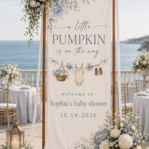 May include: A vertical fabric banner on a wooden stand featuring the text 'a little PUMPKIN is on the way', 'welcome to Sophia's baby shower', and '10.18.2026'. The design includes illustrations of a basket of pumpkins, a baby onesie, and shoes.