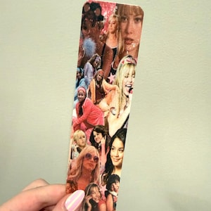 May include: A rectangular bookmark featuring a collage of images of various celebrities. The images are in shades of pink, white, and tan. The bookmark is held by a hand with pink nail polish.