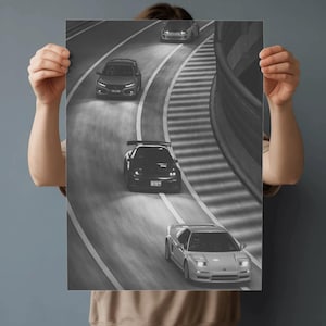 May include: Black and white print featuring a dynamic scene of several sports cars racing on a winding road. The image captures the cars in motion, with blurred streaks suggesting speed and movement. The print is held by a person.