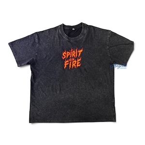 May include: A charcoal grey acid-wash t-shirt with short sleeves and a crew neckline. The center of the chest features the text "SPIRIT ON FIRE" printed in a stylized orange and red flame-like font. The fabric has a mottled, textured appearance.