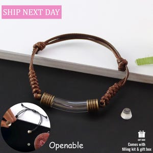 May include: A brown cord bracelet featuring a central clear glass tube with antique bronze-toned metal caps on each end. The bracelet includes adjustable sliding knots and a small, separate conical stopper piece for the glass tube component.
