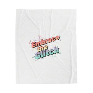 May include: White blanket featuring the phrase "Embrace the Glitch" in a colourful, pixelated font. The text is in red, yellow, green, and blue, with a black outline. The blanket has a subtle, textured pattern.