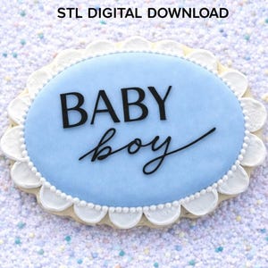 May include: An oval-shaped cookie with light blue icing and a white scalloped border. The text BABY boy is written in black on the center of the icing. Above the cookie, the text reads Baby Boy Cookie Cutter STL DIGITAL DOWNLOAD.