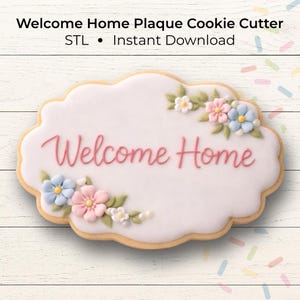 May include: A decorated cookie in the shape of a plaque with the words "Welcome Home" in pink script. The cookie is white with floral accents in pink, blue, and white. The cookie cutter is for instant download.