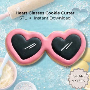 Op de afbeelding: Een koekje in de vorm van een hartjesbril met roze glazuurranden en zwarte glazen met witte accenten. De tekst Heart Glasses Cookie Cutter STL Instant Download en 1 SHAPE 9 SIZES is zichtbaar op de lichtblauwe achtergrond.