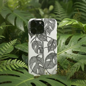 May include: A white phone case featuring a black and white illustration of monstera leaves. The case has a glossy finish and a camera cutout. The background is a lush arrangement of green leaves, creating a natural aesthetic.