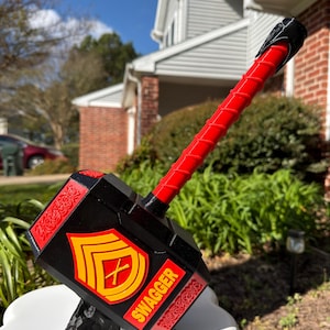 May include: A decorative hammer in black and red, with the word "SWAGGER" in red. It has a yellow and red emblem and a red handle. The hammer is displayed on a white surface.