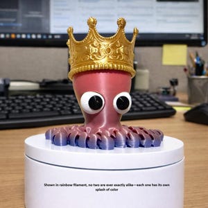 May include: A whimsical, 3D-printed octopus figurine with large, googly eyes and a gold crown. The octopus is primarily pink with blue and purple tentacles. The text at the bottom reads, "Shown in rainbow filament, no two are ever exactly alike—each one has its own splash of color."