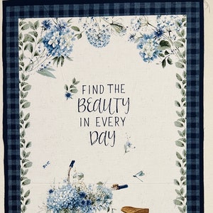 Könnte beinhalten: Ein weißes Stoffpanel mit einem blauen und weißen karierten Rand. In der Mitte des Panels befindet sich ein blaues Fahrrad mit einem Korb voller blauer Blumen. Eine Katze sitzt vor dem Fahrrad. Der Text "FIND THE BEAUTY IN EVERY DAY" ist auf dem Panel gedruckt.