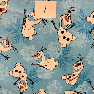 Puede incluir: Una tela azul con un patrón repetido de Olaf, el muñeco de nieve de la película Frozen. Olaf está representado en varias poses con una nariz de zanahoria y ojos negros. La tela está cubierta con un patrón de copos de nieve blancos.