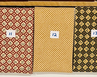 May include: Five fabric swatches with different patterns. The swatches are numbered 10 through 14. The patterns include a green and black floral design, a red and white floral design, a tan and white geometric design, a green and tan geometric design, and a tan and white floral design.